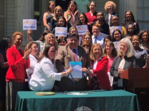 Pictured: State Rep. Camille Y. Lilly, left, celebrates the signing of a new equal pay law.